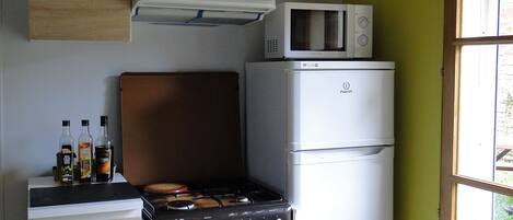 A compact kitchen with a stove, microwave, and refrigerator. There are bottles on the counter, and a window provides natural light.