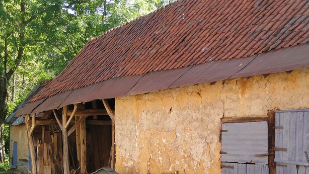 Een rustiek gebouw met een verweerde buitenkant, een houten constructie met een schuin dak en een kleine ingang.