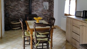 Een eethoek met een stenen openhaard, houten balken in het plafond, een betegelde vloer en een raam met gordijnen.