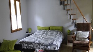 Een slaapkamer met een bed, een stoel, een tafel en een trap.