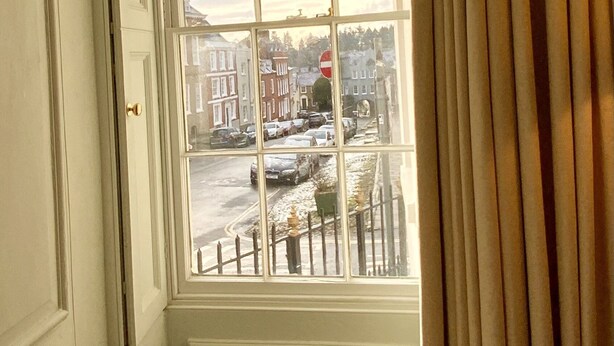 Une pièce dotée d’une grande fenêtre, d’un canapé beige et donnant sur une rue bordée de voitures garées et d’immeubles.