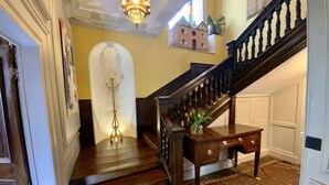 Un magnifique escalier en bois, doté d’une rampe et d’une balustrade sombre, mène à un palier où se trouvent un vase de fleurs et une petite table.