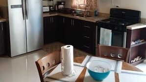 Ett kök med mörka träskåp, ett kylskåp i rostfritt stål, en spis och ett matbord med stolar.