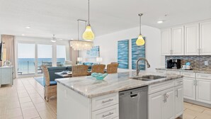 A modern kitchen with white cabinets, a central island with a sink, and a dining area with wicker chairs.