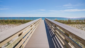 A wooden boardwalk leading to a beach with clear blue water and a clear sky.