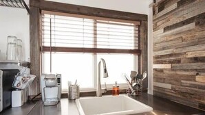 Una cocina moderna con un lavamanos de acero inoxidable, una cafetera y una ventana con persianas.