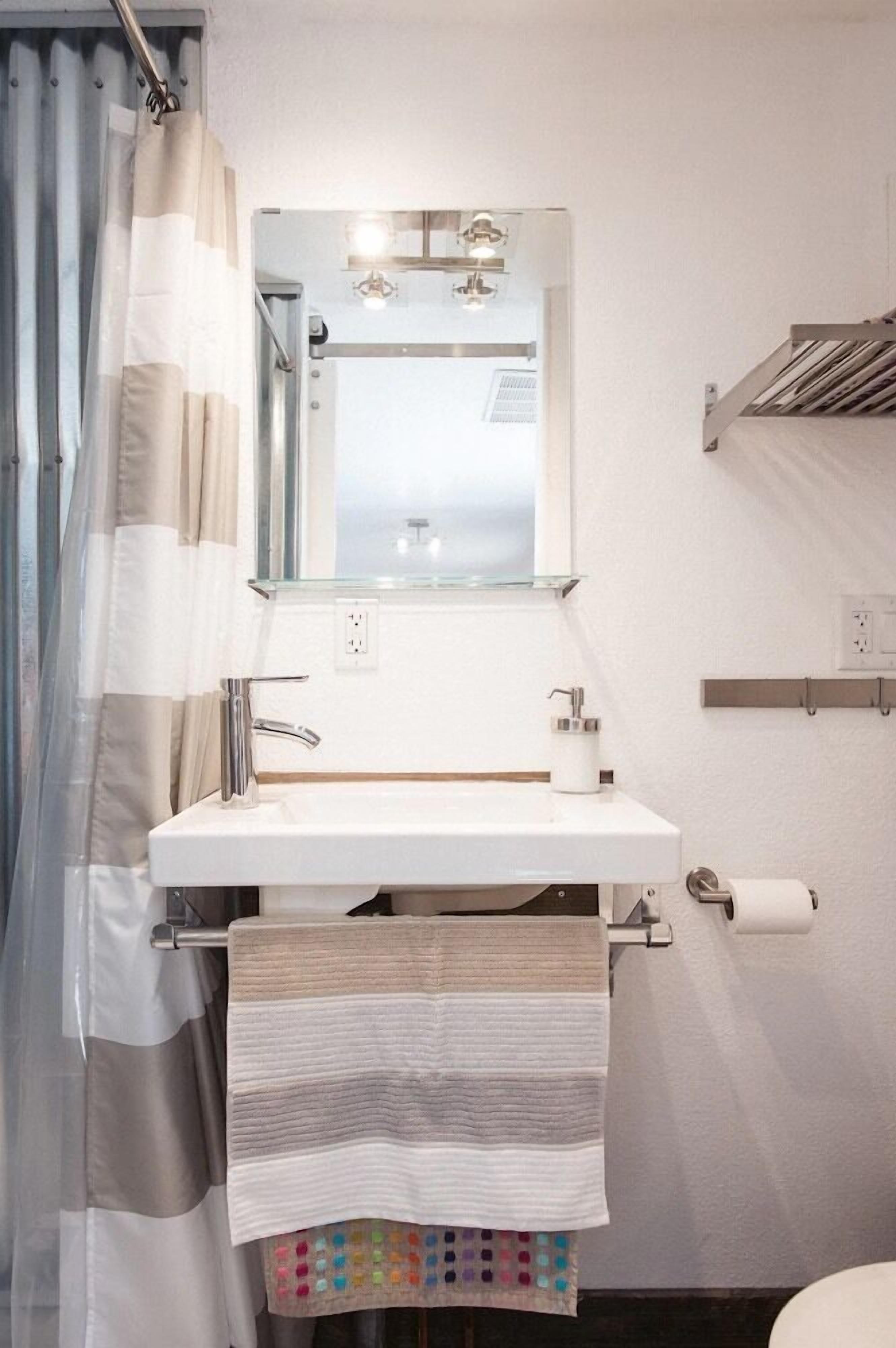 A bathroom with a white sink, a mirror, a towel rack, and a toilet paper holder.