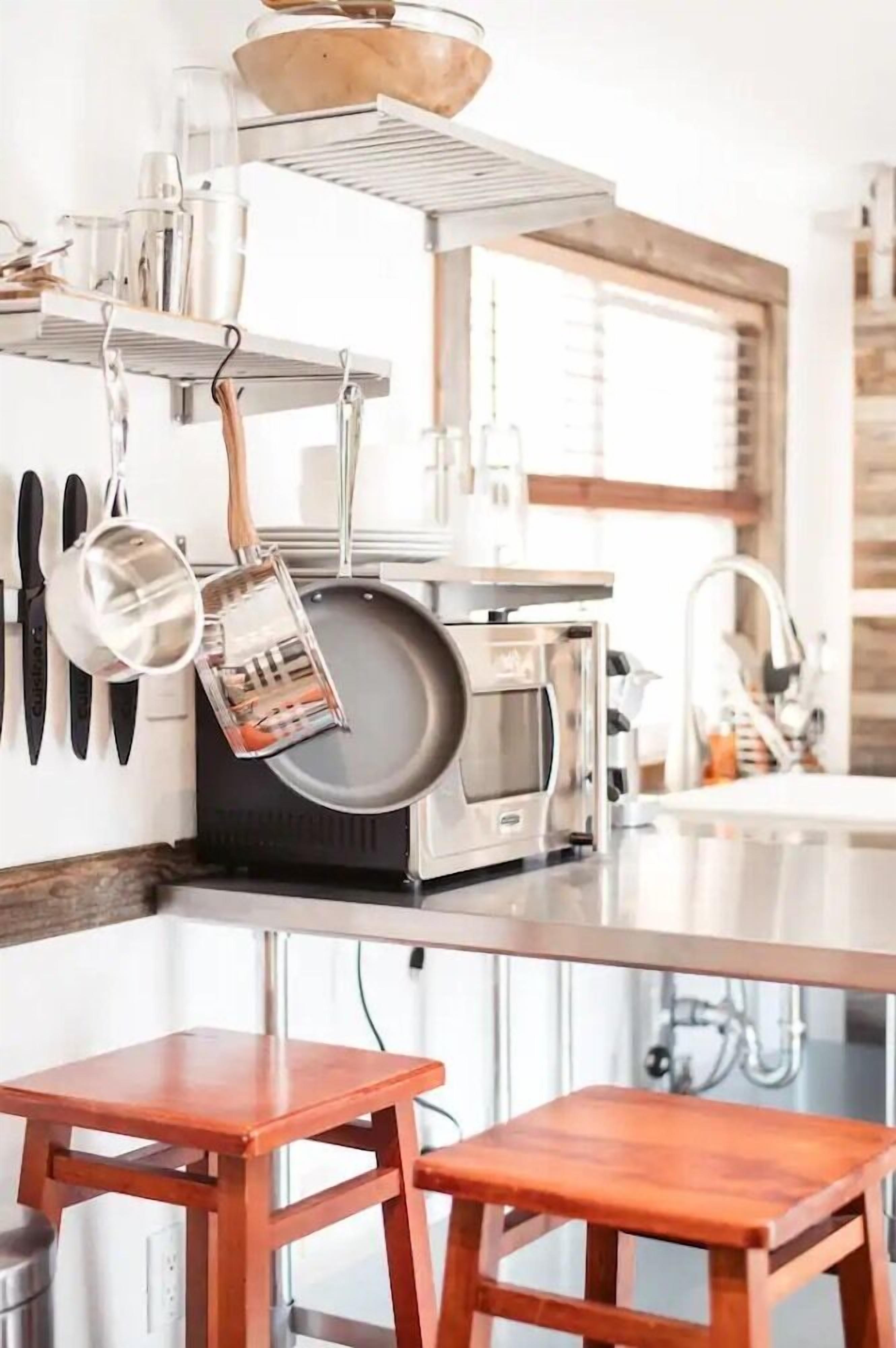 A kitchen with a microwave, a frying pan, and a wooden stool.