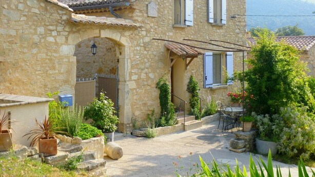 A stone house with a tiled roof, a covered porch, and a garden with potted plants and a table. - SPACIOUS GITE FOR 4 PEOPLE IN AUTHENTIC PROVENCAL FARMHOUSE (Suzette)