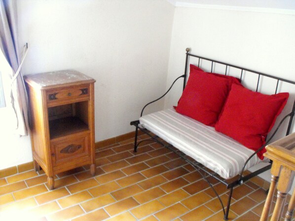 A small room with a metal bed frame, a wooden nightstand, and a tiled floor.