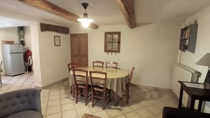 A dining area with a round table and chairs, a ceiling fan, and a kitchen in the background. - SPACIOUS GITE FOR 4 PEOPLE IN AUTHENTIC PROVENCAL FARMHOUSE (Suzette)