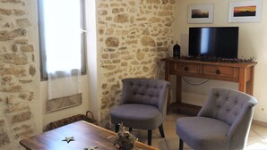 A living room with a stone wall, two grey upholstered chairs, a wooden table, and a TV on a wooden cabinet. - SPACIOUS GITE FOR 4 PEOPLE IN AUTHENTIC PROVENCAL FARMHOUSE (Suzette)