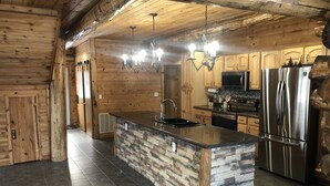 Una cocina moderna con paredes de madera, una isla de piedra, electrodomésticos de acero inoxidable y una araña.