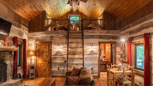 A log cabin interior with a loft bedroom, a fireplace, and a dining area. - The Wilderness Lodge at Four Fillies Lodge w/ Hot Tub (Peterstown)