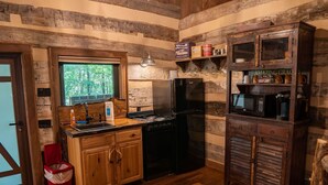 A rustic kitchen with wooden cabinets, a black refrigerator, a stove, and a microwave. - The Wilderness Lodge at Four Fillies Lodge w/ Hot Tub (Peterstown)