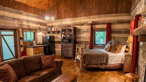 A rustic cabin interior with a wooden floor, a sofa, a bed, a dining table, and a kitchen area. - The Wilderness Lodge at Four Fillies Lodge w/ Hot Tub (Peterstown)