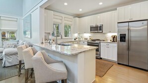 Une cuisine moderne avec des meubles blancs, un réfrigérateur en acier inoxydable, un four à micro-ondes et un grand îlot central doté de tabourets de bar.