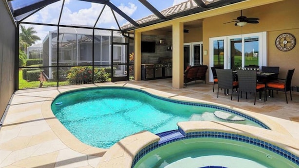 A swimming pool with a hot tub, outdoor seating, and a covered patio area. - Luxurious home with stunning golf course views and private swimming pool & spa (Naples)