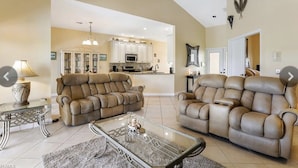 A spacious living room with a sofa and armchair, a glass coffee table, and a ceiling fan. - Luxurious home with stunning golf course views and private swimming pool & spa (Naples)