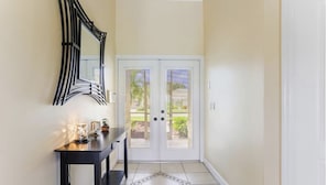 A hallway with a black console table, a decorative mirror, and a double door leading outside. - Luxurious home with stunning golf course views and private swimming pool & spa (Naples)