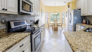 A kitchen with granite countertops, stainless steel appliances, and a dining area with a table and chairs. - Luxurious home with stunning golf course views and private swimming pool & spa (Naples)