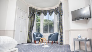 A room with a corner window, two leather armchairs, a small table, a bed, and a television on the wall. - The Woodside Hotel, Aberdour. Exclusive Use (Burntisland)