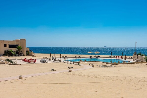 A pool area with lounge chairs and umbrellas, a clear blue sky, and a view of the sea.
