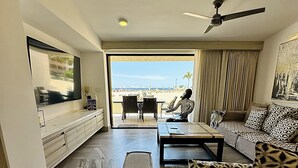 Un salon spacieux doté d’un grand téléviseur à écran plat, d’un ventilateur de plafond et offrant une vue sur la plage grâce à une porte-fenêtre coulissante.