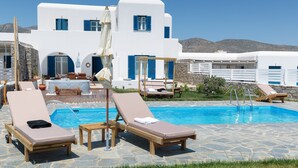 A poolside area with lounge chairs, a table, and a stone-tiled deck. - Villa Olena: 2 villas 10 pax 2 pools Punda Beach Paros (Paros)