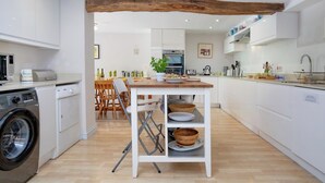 A modern kitchen with white cabinetry, a wooden table, and a hanging wooden beam. - Spacious,  Well Equipped Cottage Near South  Devon coast - Sleeps 10 (plus2) (Slapton, Near Kingsbridge)