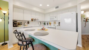Una cocina moderna con armarios blancos, una isla central con taburetes, microondas y refrigerador.