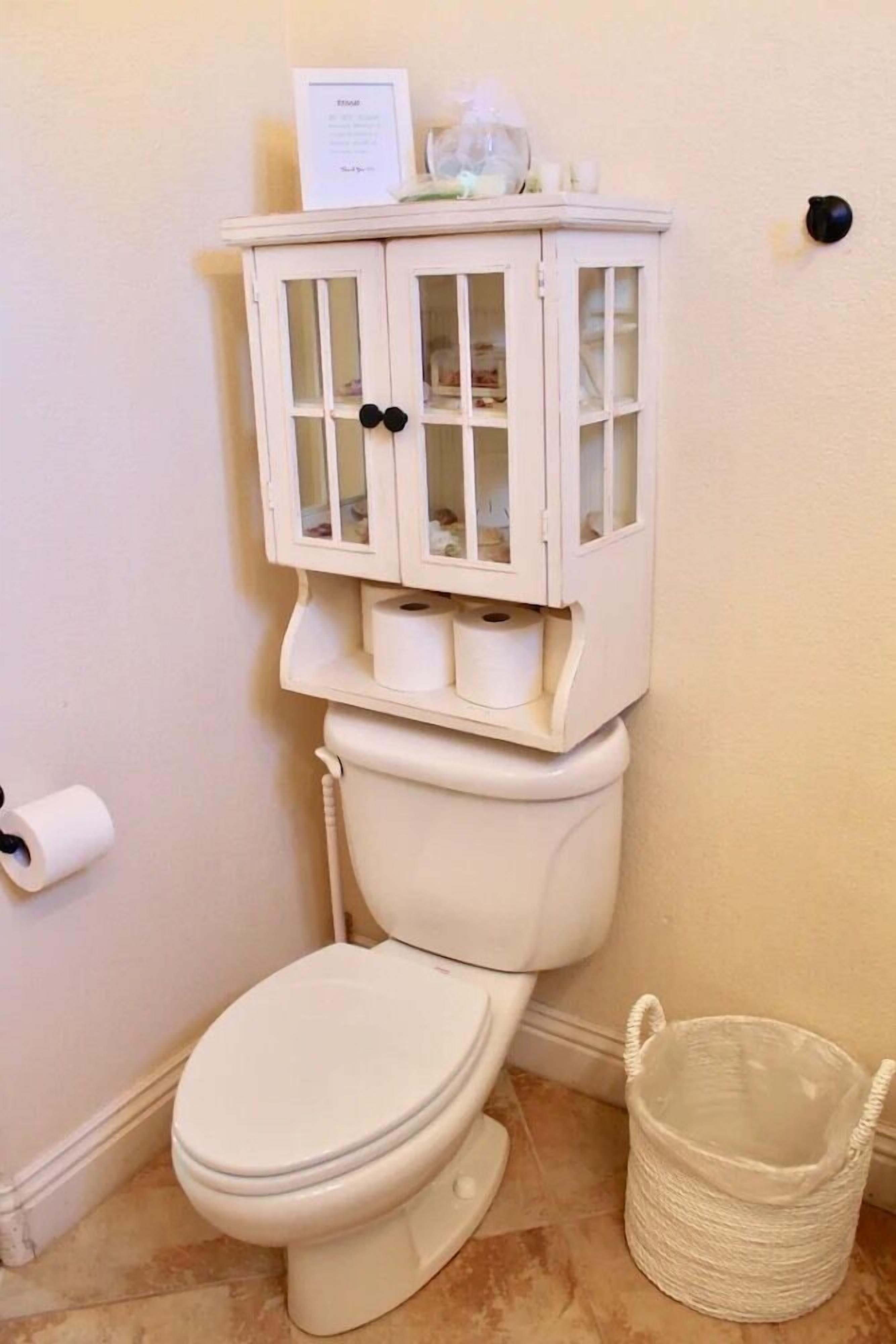 Des toilettes avec un meuble au-dessus, un rouleau de papier toilette et une poubelle.