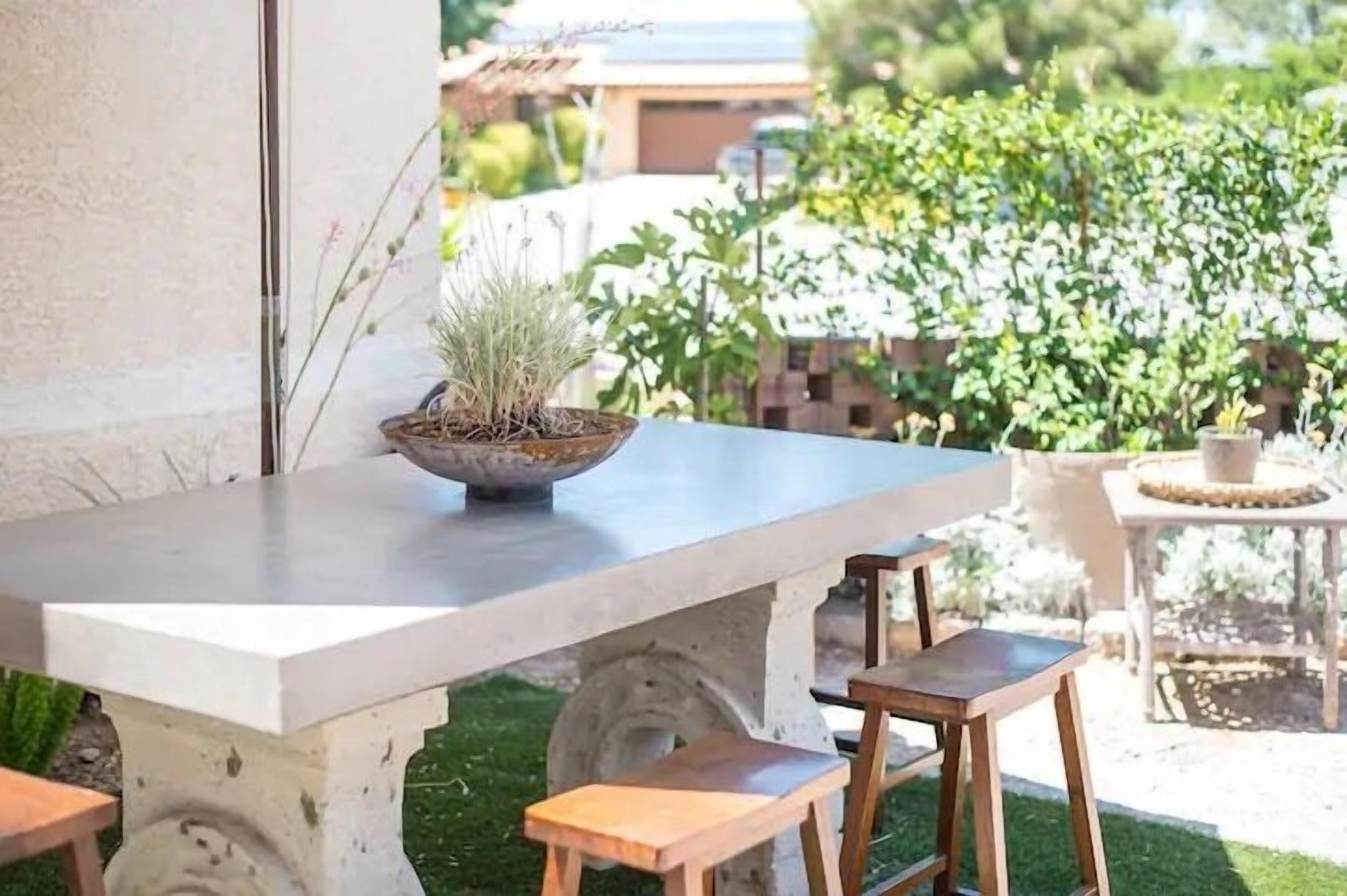 A concrete table with a potted plant, wooden stools, and a small round table with a woven base.