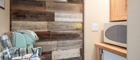 A kitchen with a rustic wooden wall, a microwave, and a refrigerator.