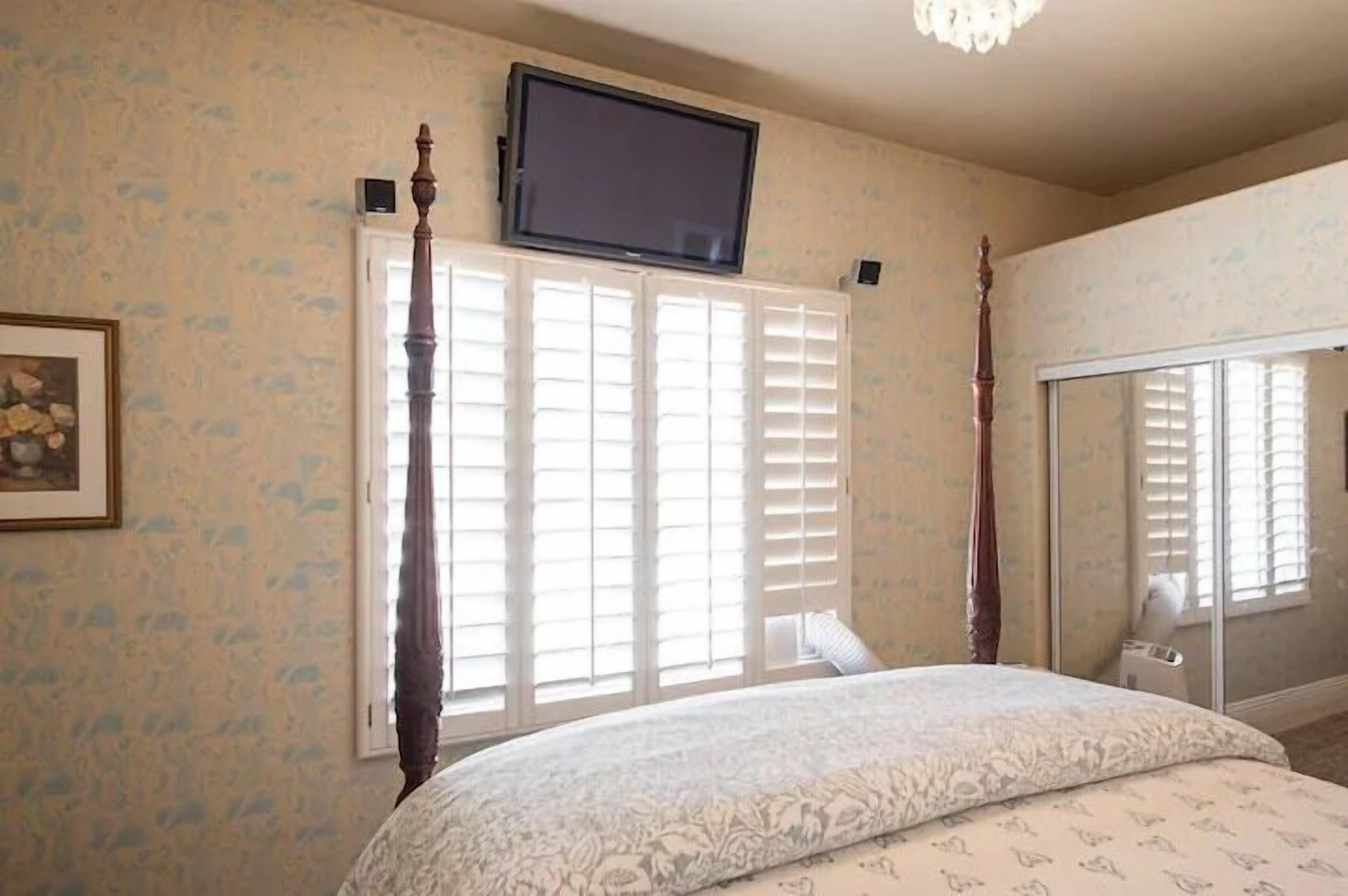 Une chambre à coucher avec un lit à baldaquin, un téléviseur fixé au-dessus du lit et un grand miroir sur le mur.