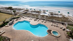 A pool area with a large pool and a hot tub, surrounded by lounge chairs and a deck.