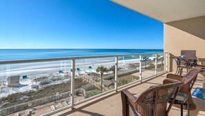 A balcony with wicker furniture overlooking a beach.