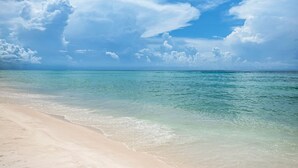 A beach with clear turquoise water and a sandy shore under a partly cloudy sky.