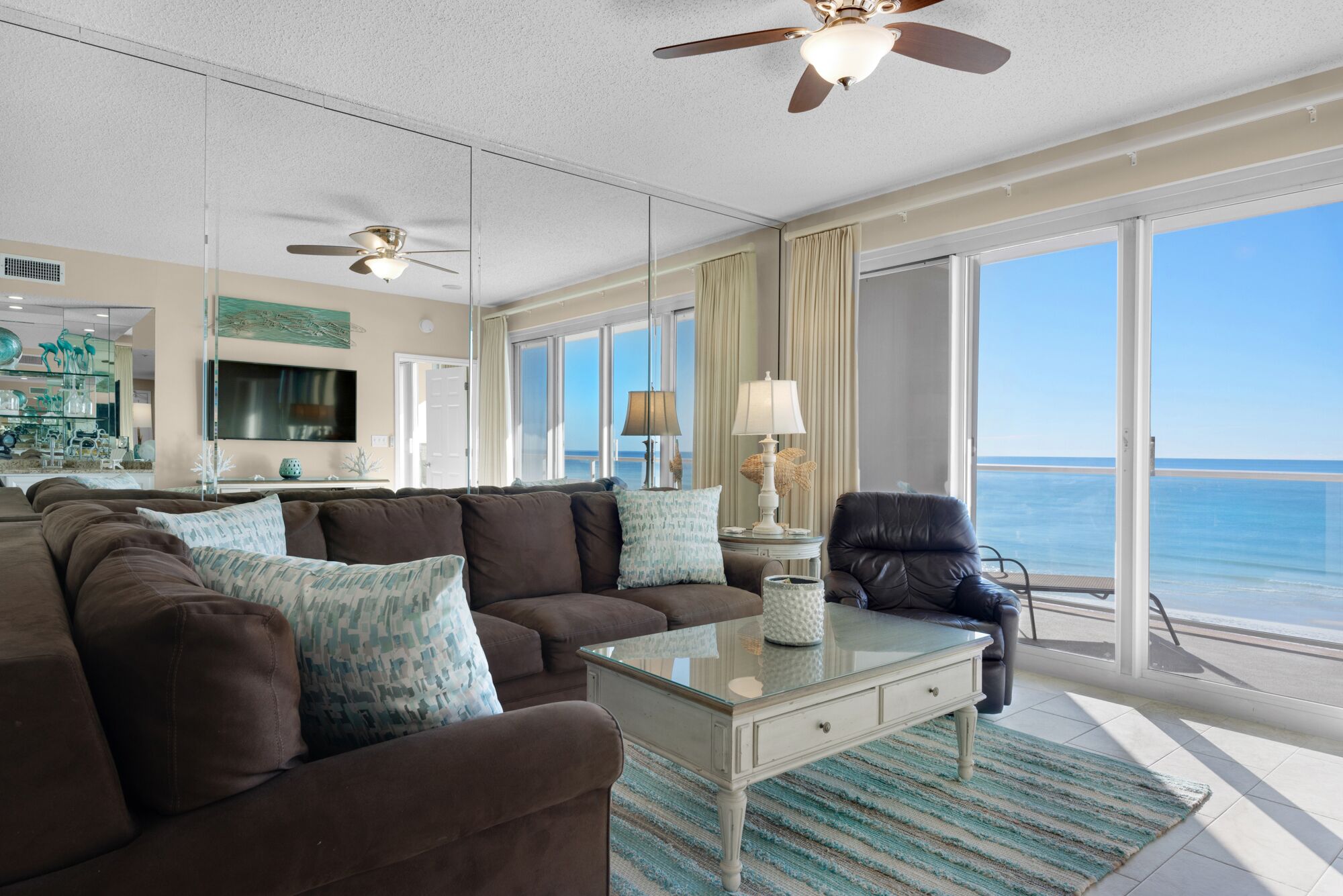 A spacious living room with a large brown sofa, a glass coffee table, and a view of the ocean through large windows.