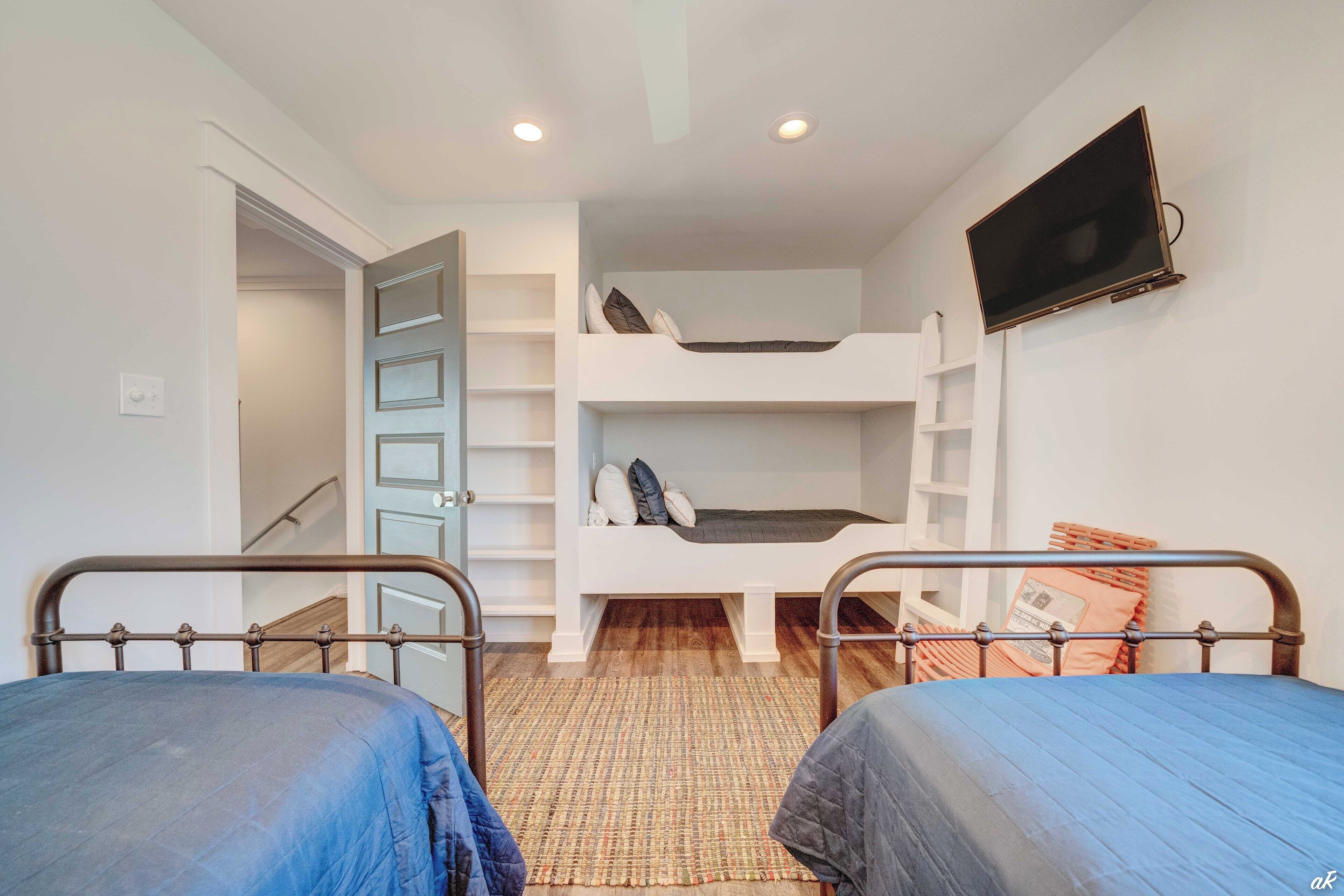 A dorm-style room with bunk beds, a flat-screen TV, and a small window.