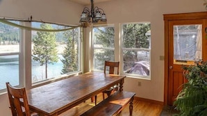 A dining area with a wooden table and benches, large windows with a view of a lake and trees, and a door with a window.