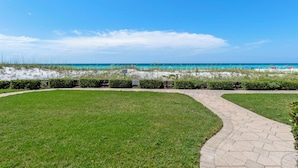 Un sentier pavé mène à une plage bordée d’une eau d’un bleu limpide.