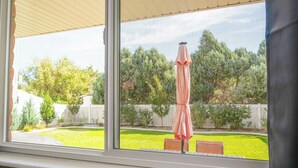 A view through a window of a backyard with a lawn, a wooden fence, and a red and white umbrella.