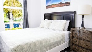A neatly made bed with a patterned bedspread, a dark wooden headboard, and a nightstand with a lamp.
