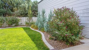 A well-maintained backyard with a lawn, a variety of shrubs, and a wooden deck.