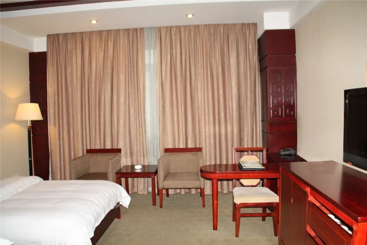 A hotel room with a bed, two armchairs, a small table, a TV, and a wardrobe.