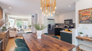A modern kitchen with a central island, a dining area with a wooden table and green chairs, and a chandelier. - Tri-level condo, close to Coonskin Lift! (Telluride)