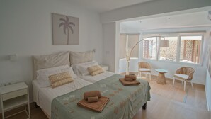 A spacious bedroom with a large bed, a nightstand, a chair, and a table.