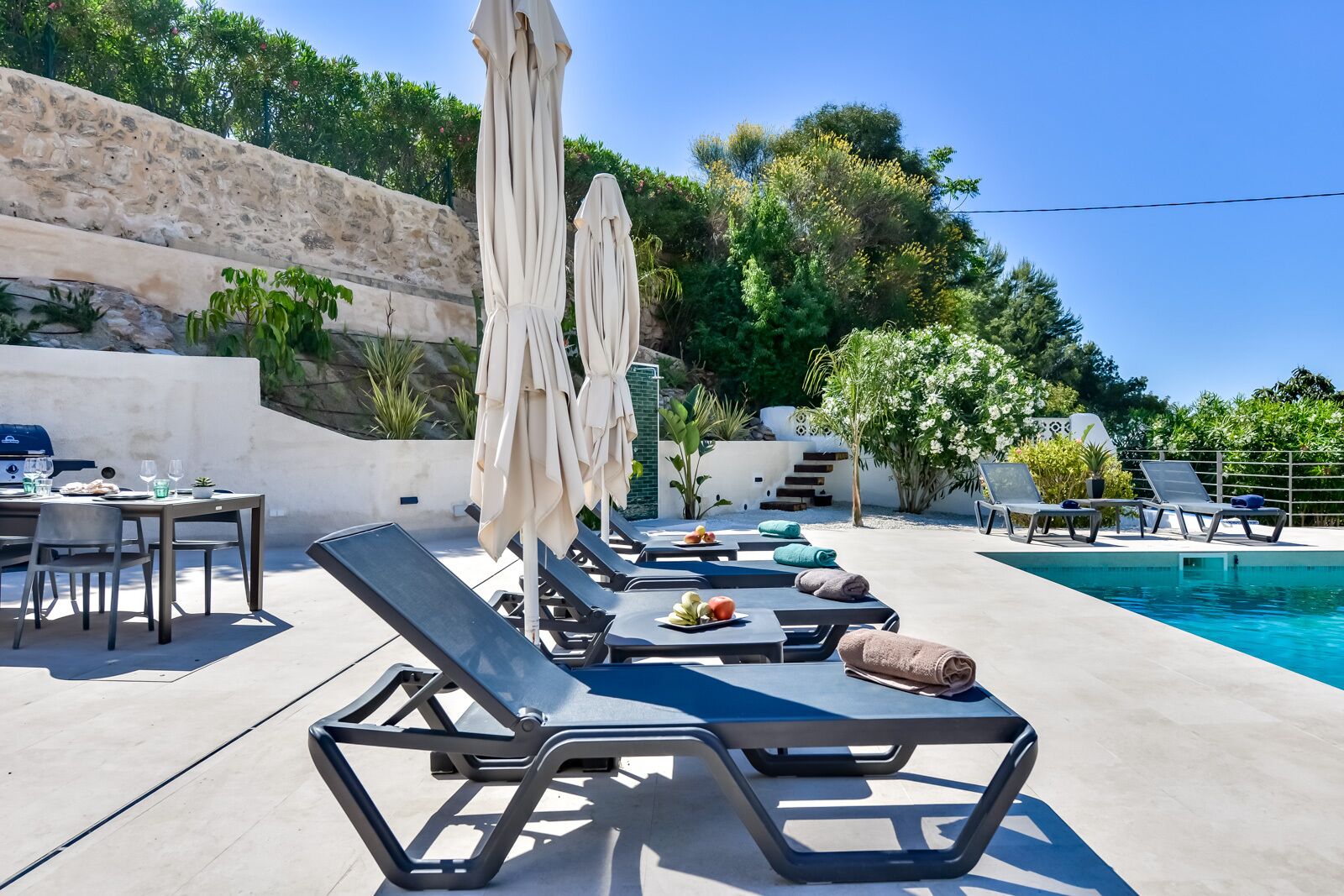 Ein Poolbereich mit Liegestühlen, Sonnenschirmen und einem Grill.