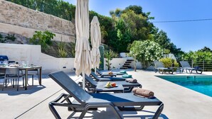 A poolside area with lounge chairs, umbrellas, and a barbecue grill.